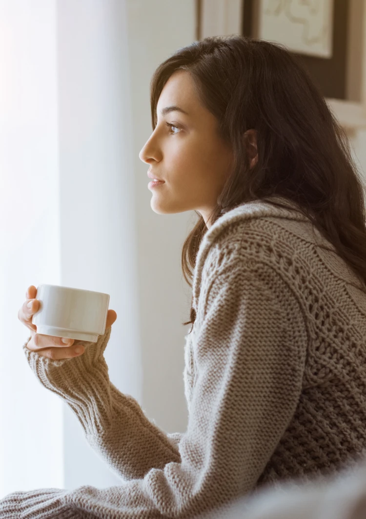 Women drinking a cup of coffee and looking out of the window.